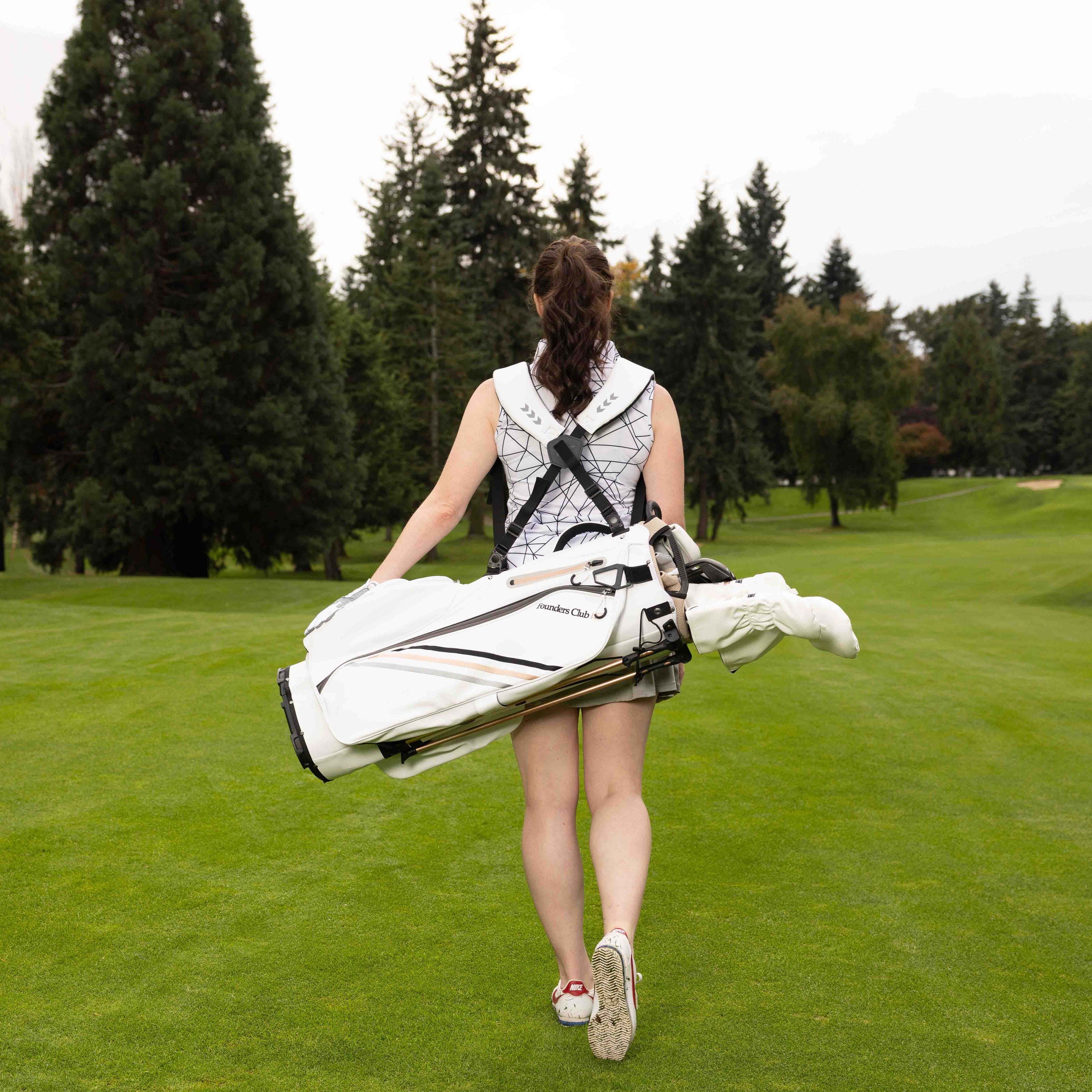 Woman walking on a golf course carrying a white golf bag.