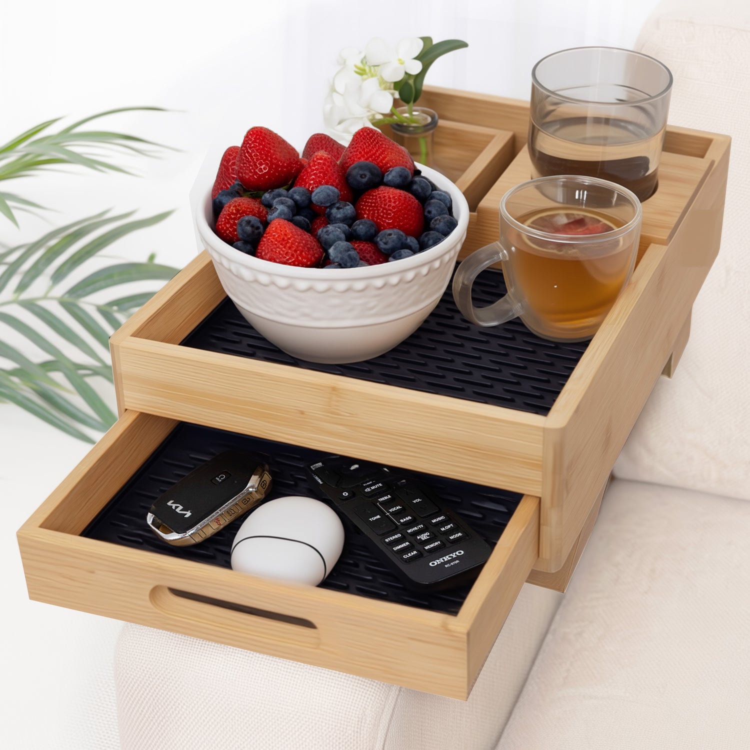 Wooden tray with a bowl of berries, cups of tea, and remote controls on a couch.