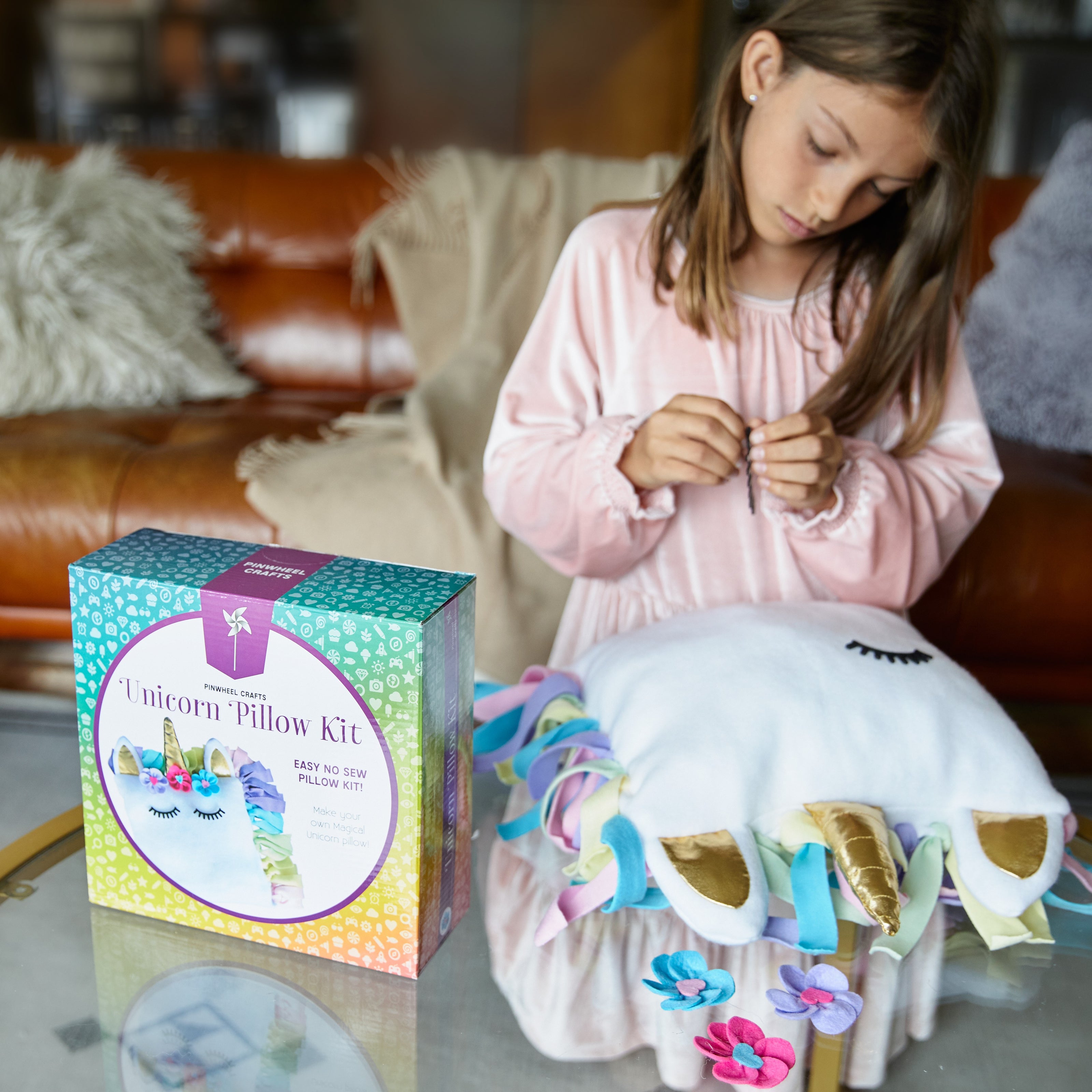 Girl making a unicorn pillow with a completed unicorn pillow and kit box on a table.