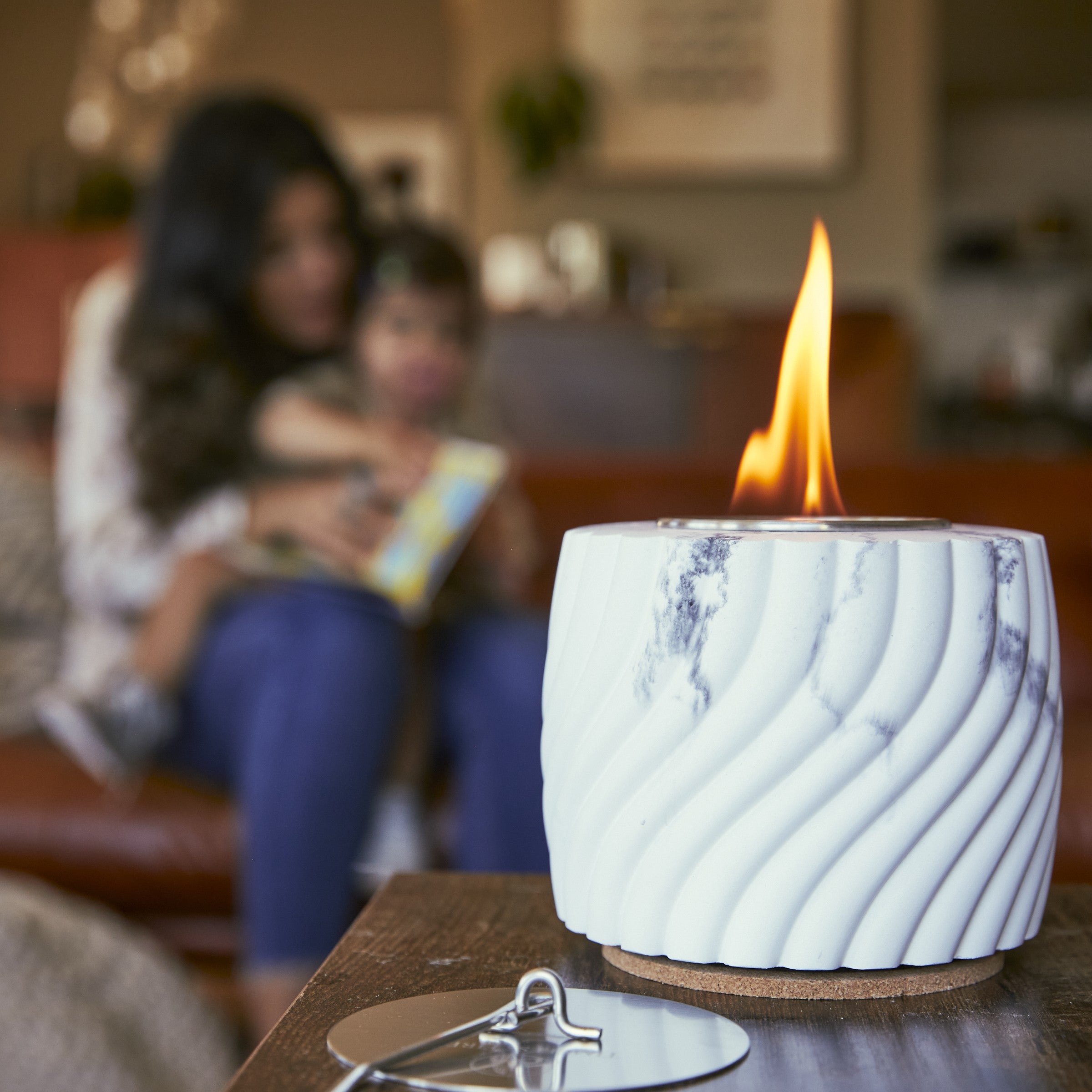 Marble-patterned candle with a flame on a table, blurred background of people reading a book.